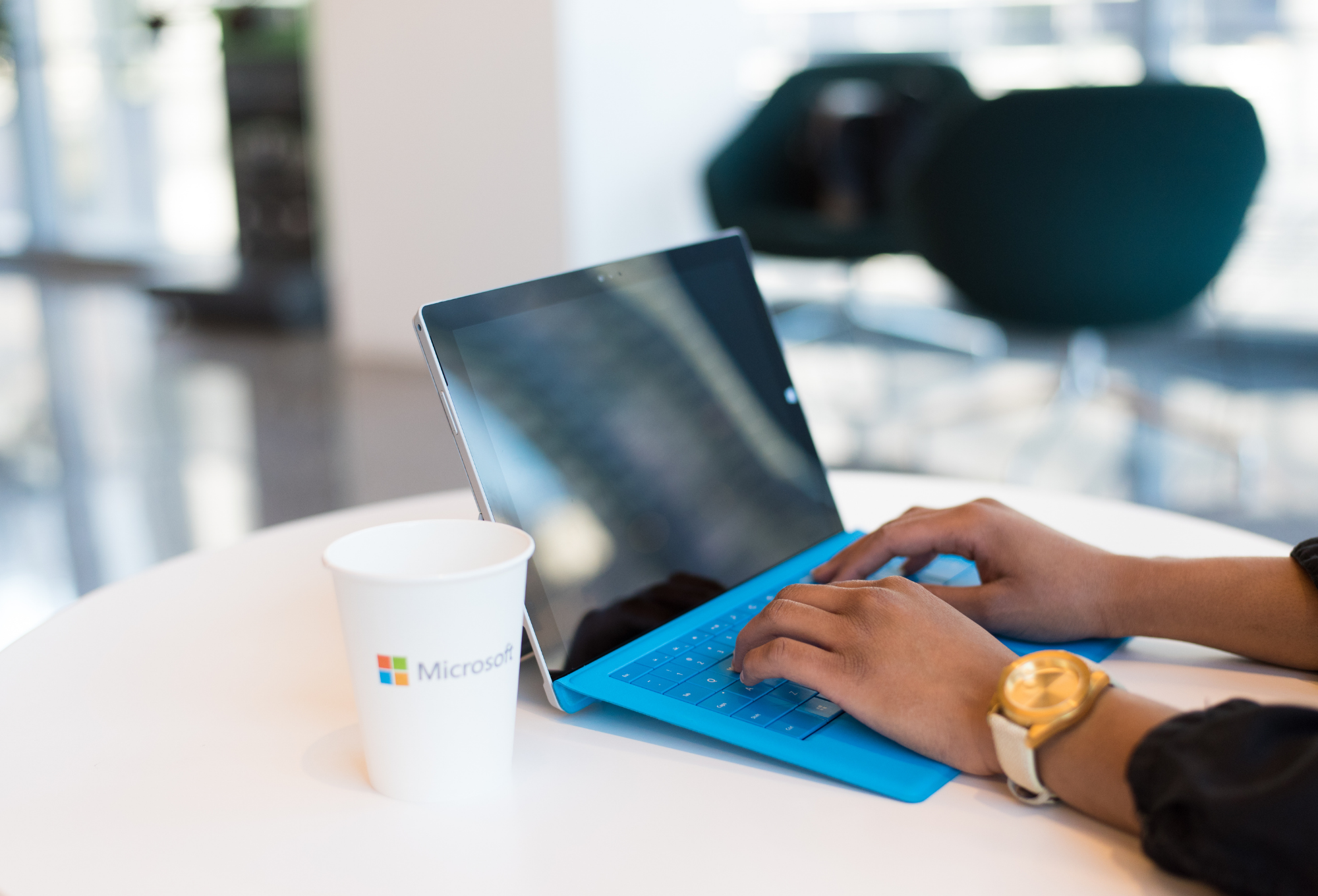 Widok z boku na osobę pracującą na laptopie przy papierowym kubku kawy z napisem Microsoft – symbol nowoczesnej pracy zdalnej i cyfrowego stylu życia.